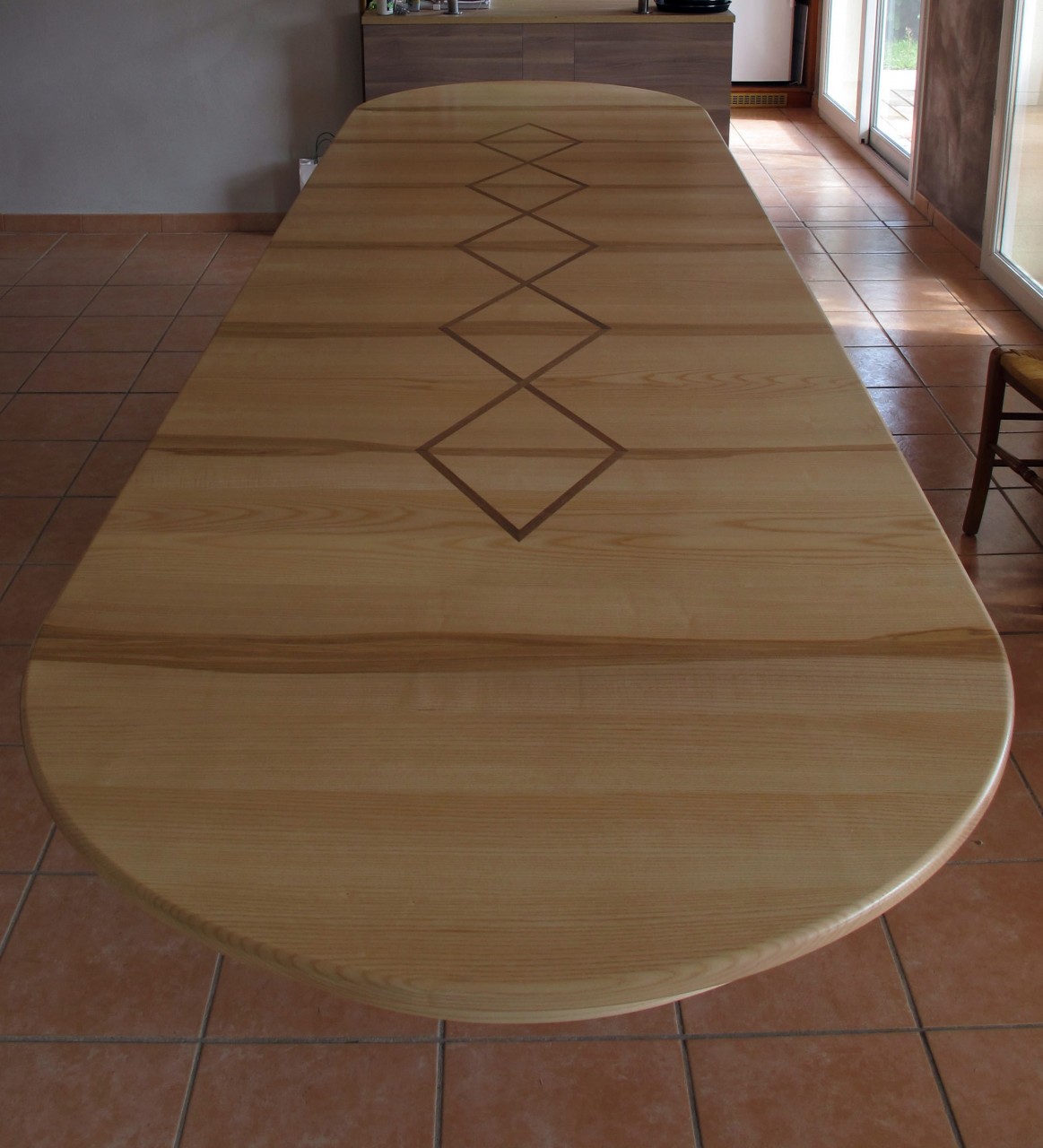 Une incrustation de placage en Noyer décore le plateau de la table. En plus le motif ce prolonge sur les rallonges.