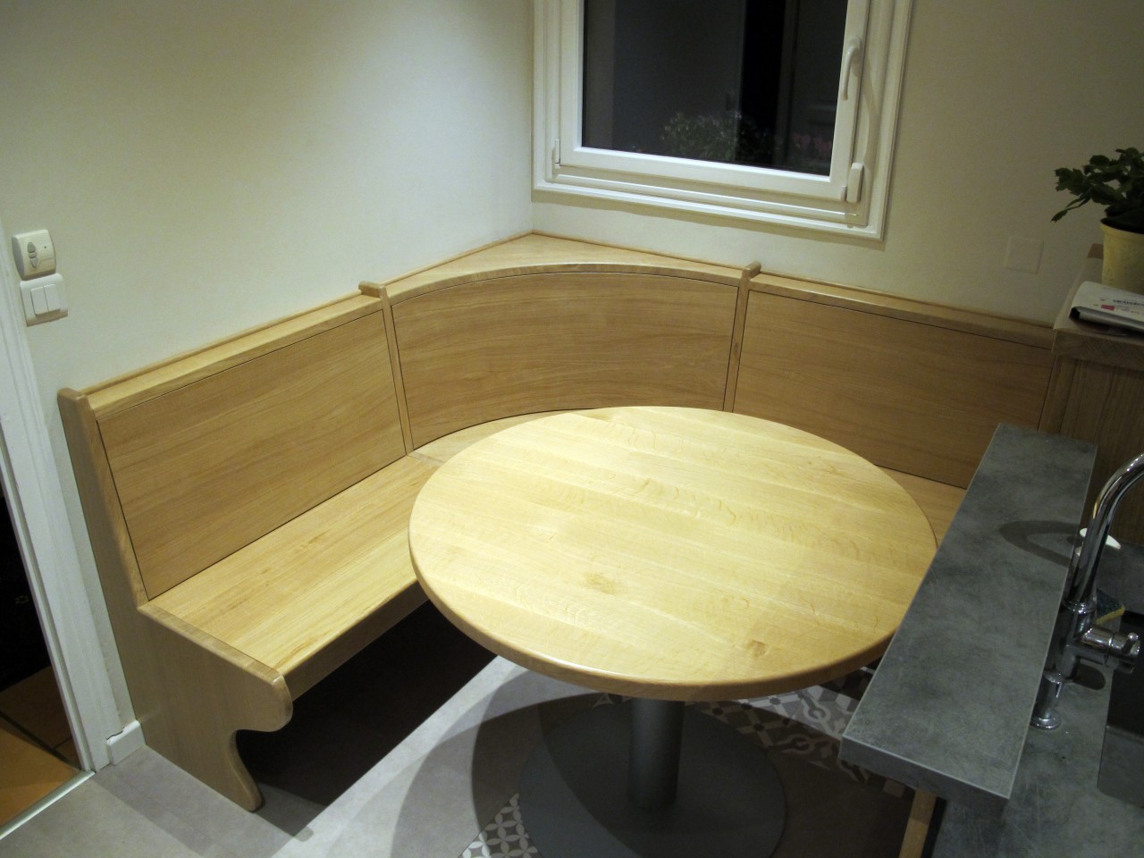 La banquette d'angle et la table ronde en chêne dans leur globalité. Elles permettent de créer un espace conviviale dans la cuisine.