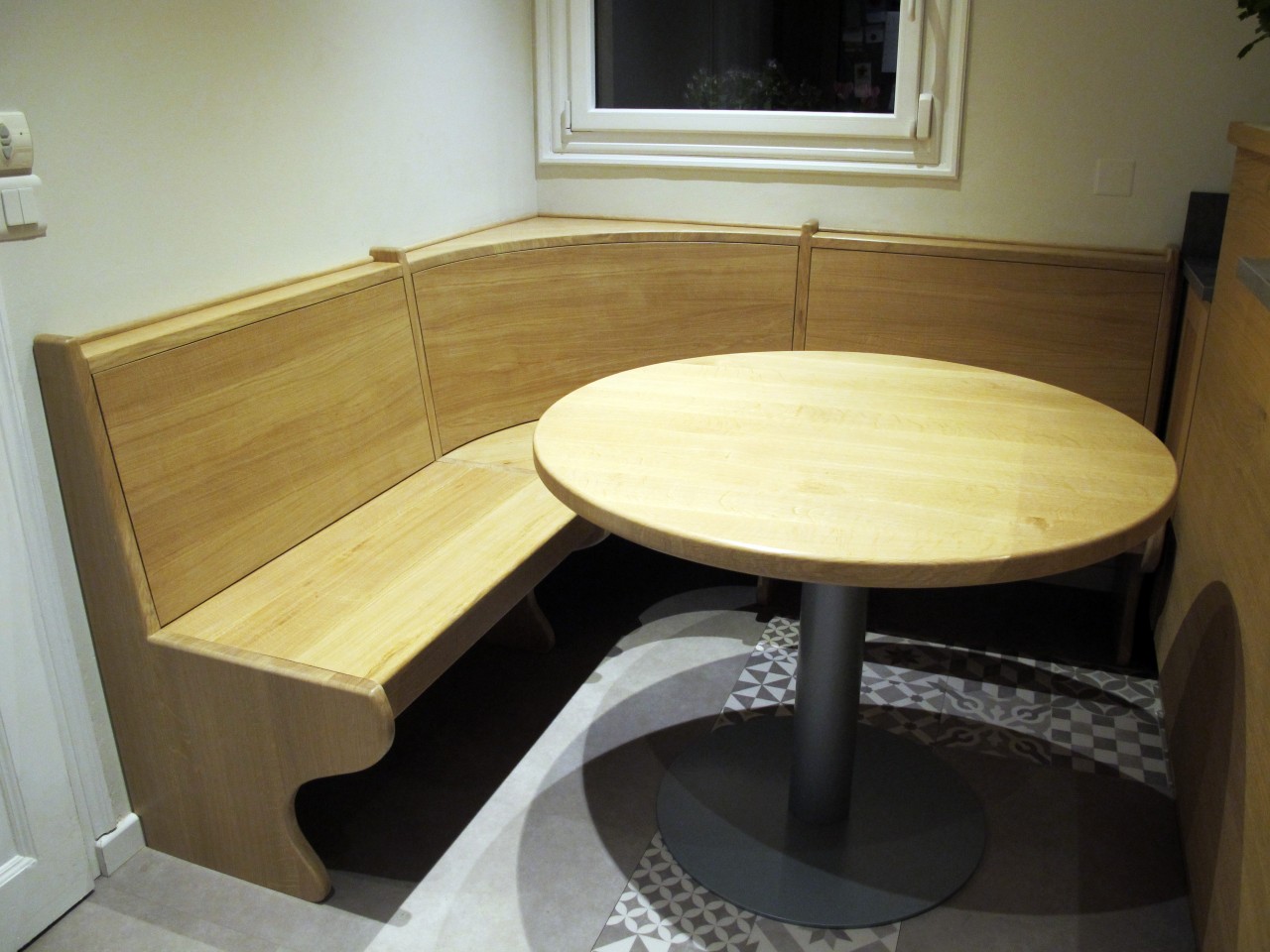 La table en chêne massif supporté par un pied central en acier prend place au centre de la banquette.